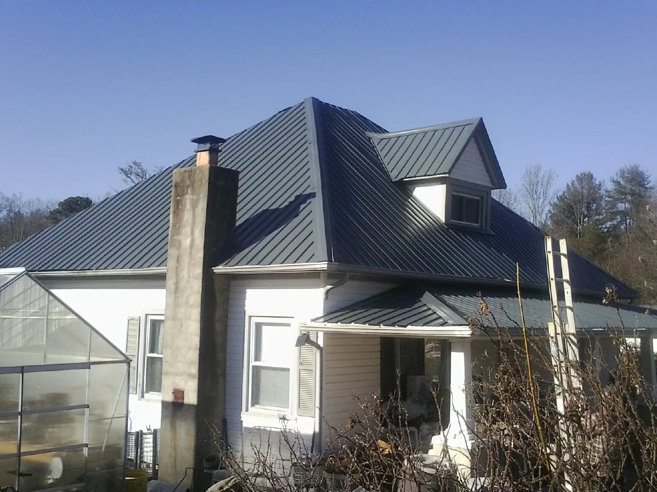 Dark blue standing seam metal roof on a white farmhouse with dormer — Slate & Tile Roof Repair by Roofing Brothers in Oak Island