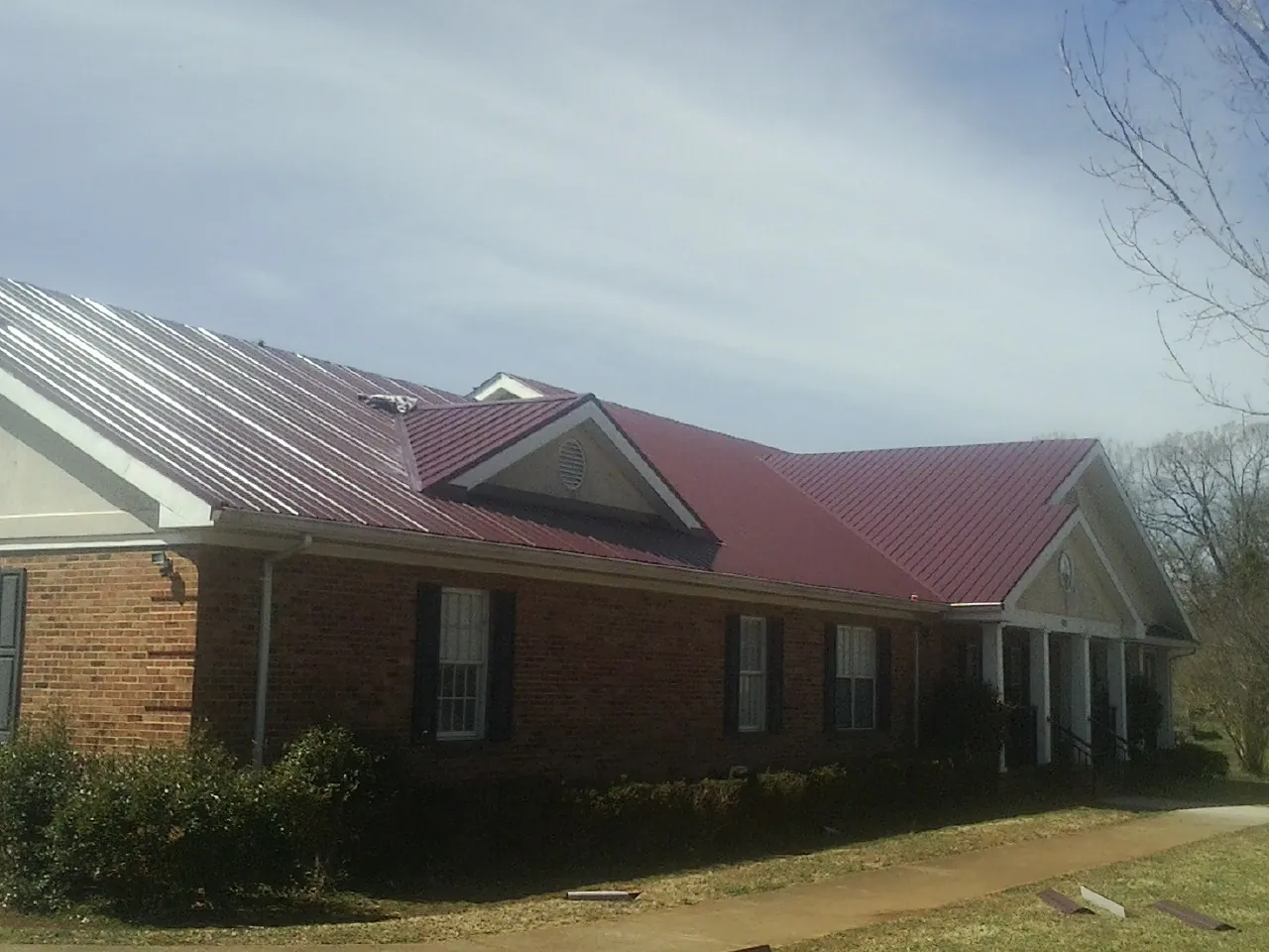 Red metal roof with gabled entries on a long brick building, from a Hail Damage Roof Repair job in Oak Island