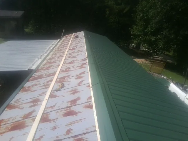 Old rusted panels beside newly installed green metal roofing — Wind Damage Roof Repair by Roofing Brothers in Oak Island