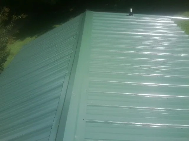 New green metal panels meeting at the ridge of a roof — Flat Roof Repair work by our crew in Oak Island