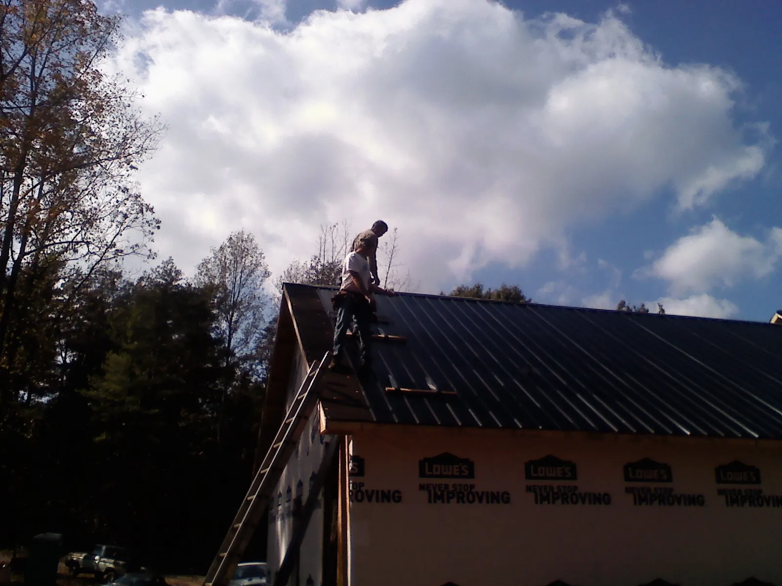 Roofer fastening dark metal panels high against a cloudy sky, from a Roof Inspection job in Oak Island
