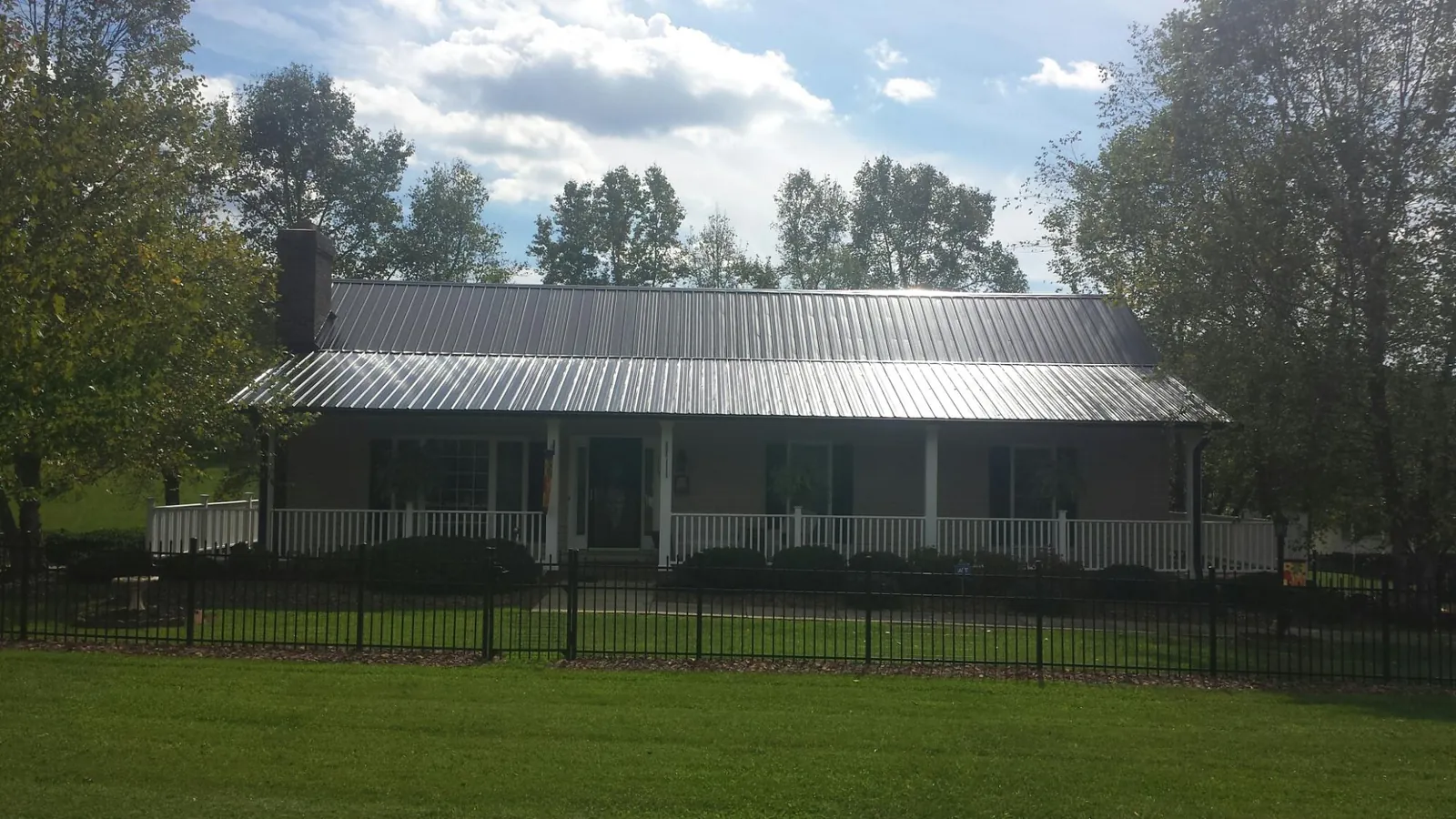 Gray metal roof on a brick ranch with a full width front porch — Gutter Guard Installation work by our crew in Oak Island