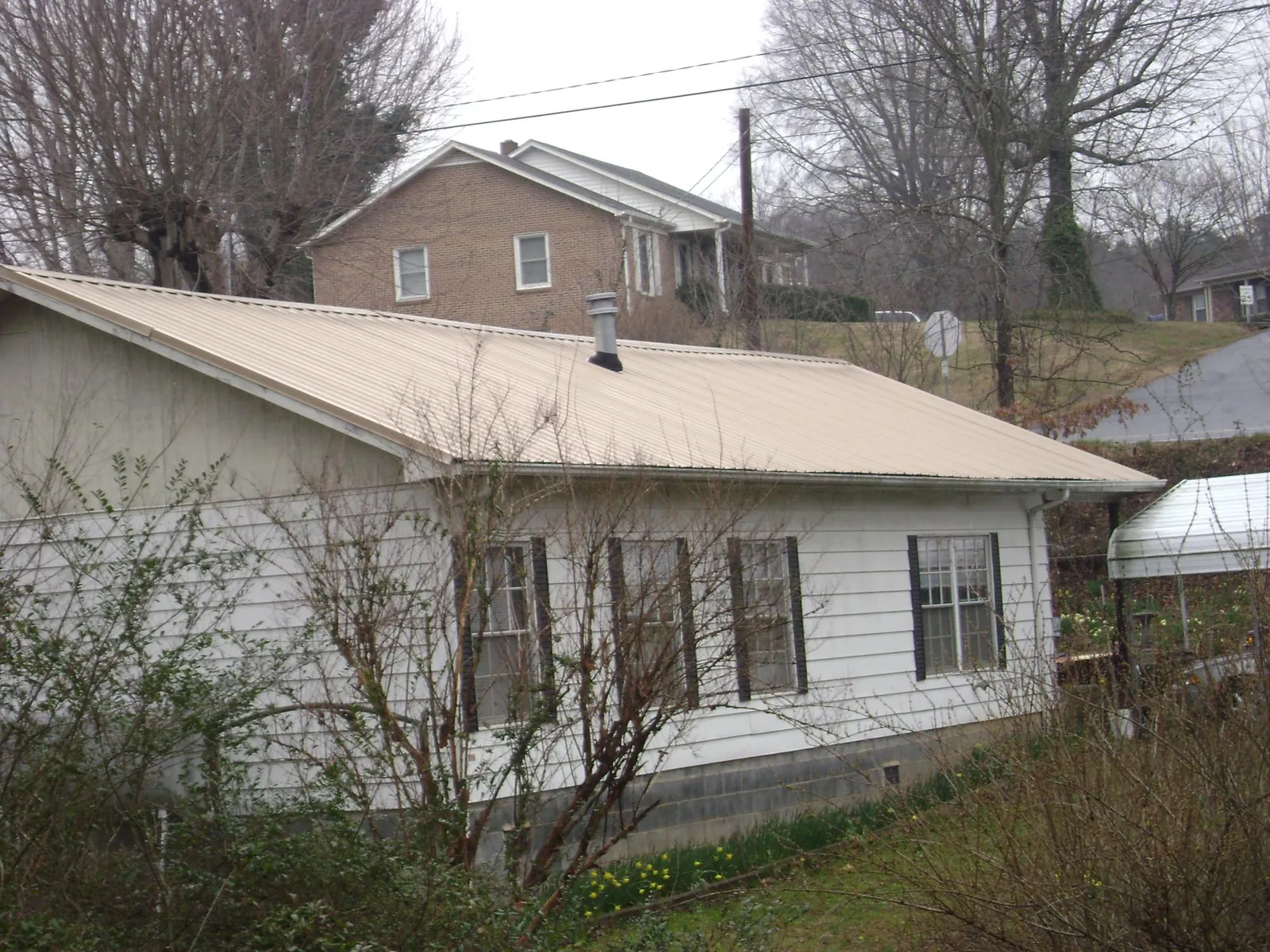 Tan metal roof on a white sided house set into a hillside — Commercial Roofing by Roofing Brothers in Oak Island