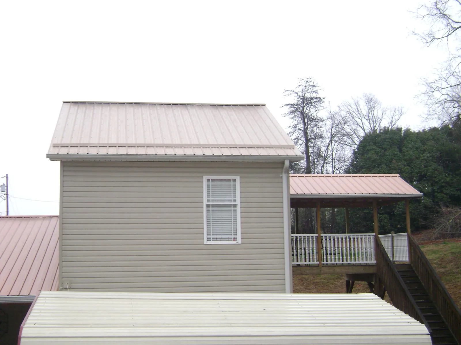 Tan metal roofs on a two story addition and attached porch, from a Roof Replacement job in Oak Island